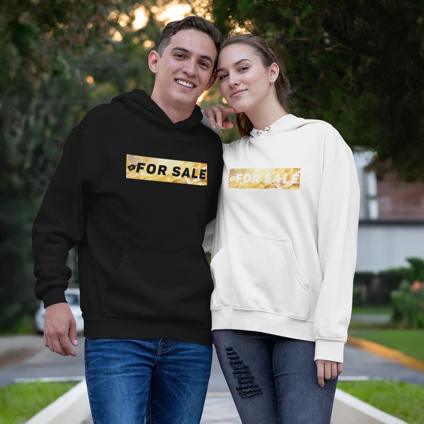 Herr mit schwarzem Hoodie und Dame mit weißem Hoodie. Die Hoodies sind jeweils mittig mit dem Schriftzug "FOR SALE" als klare Aussparung versehen.